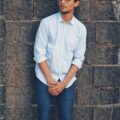 Stylish young man with eyeglasses posing against a brick wall outdoors.